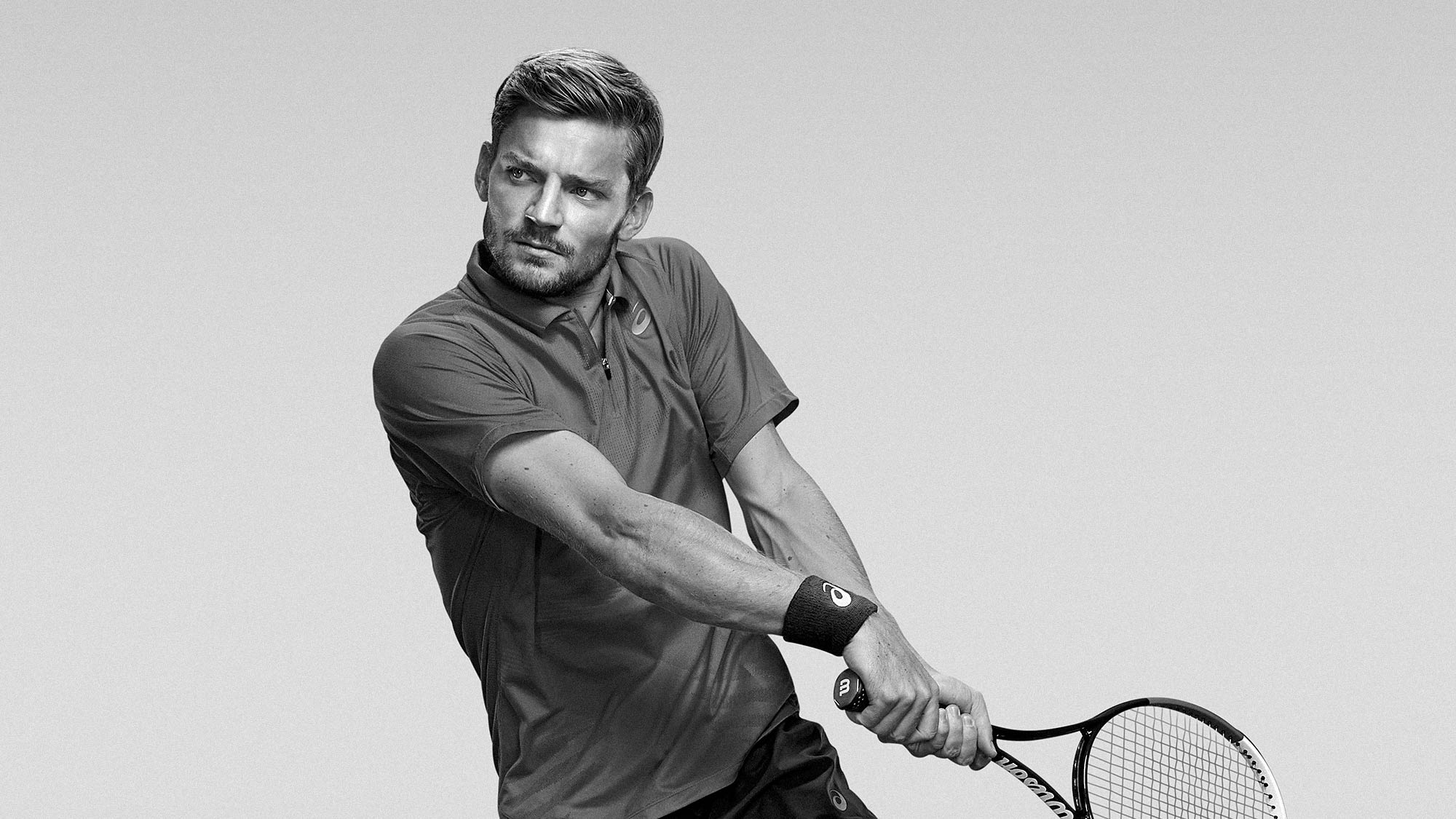 Action image of David Goffin leaping into a back hand tennis shot. Commercial imagery for ASICS Europe